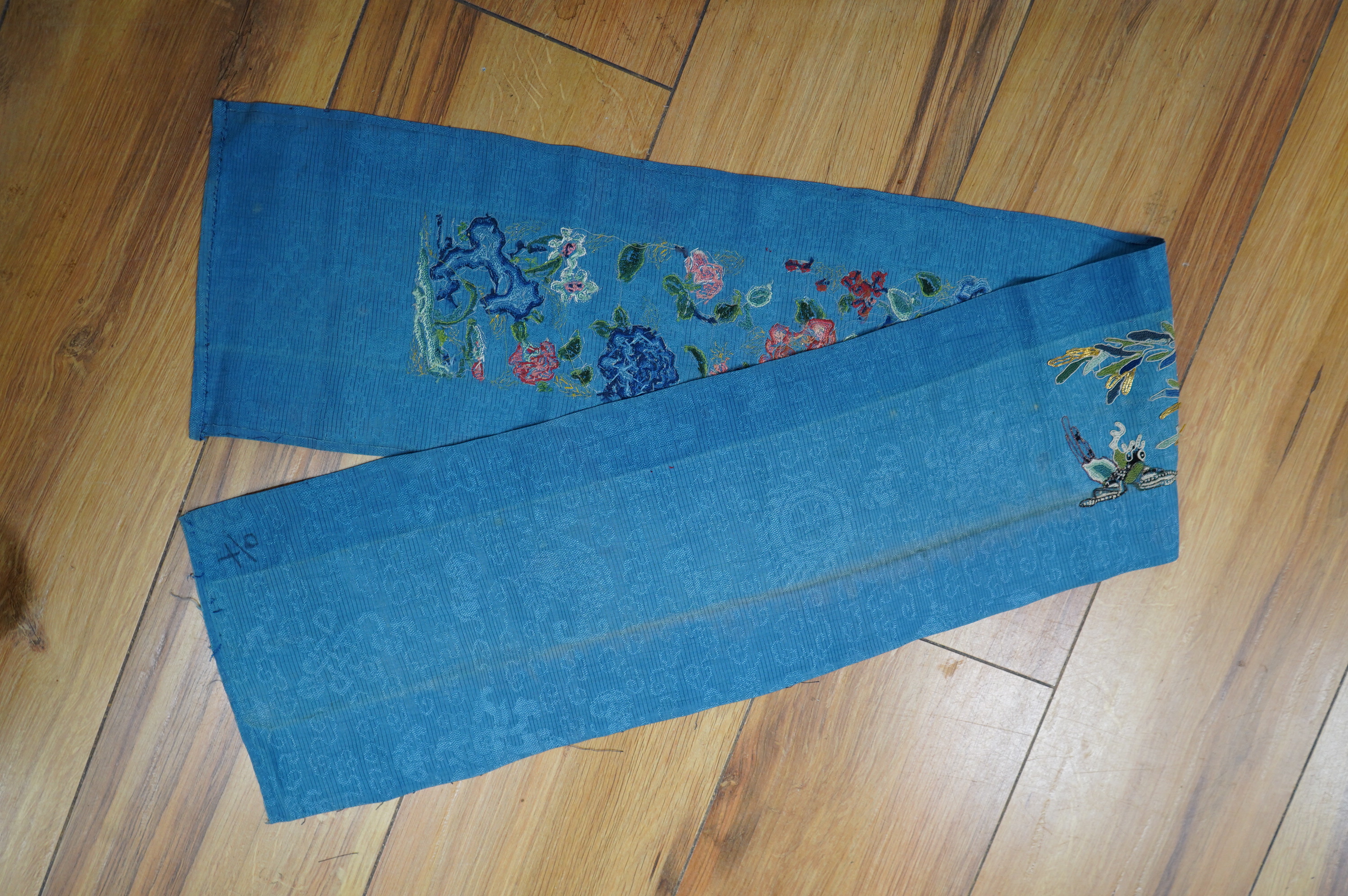 A 19th century Chinese blue silk embroidered sleeve band, embroidered in multi-coloured silk and gold thread, mostly worked in Chinese knot, in a floral and bat design, 48cm long, unframed., Condition - good